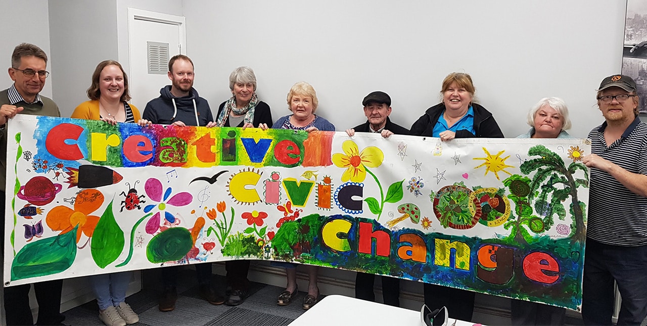 A group holding a handmade sign that says 'Creative Civic Change'