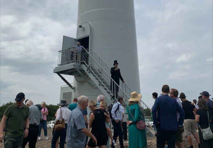 The bottom of a wind turbine and a group of people standing around it.