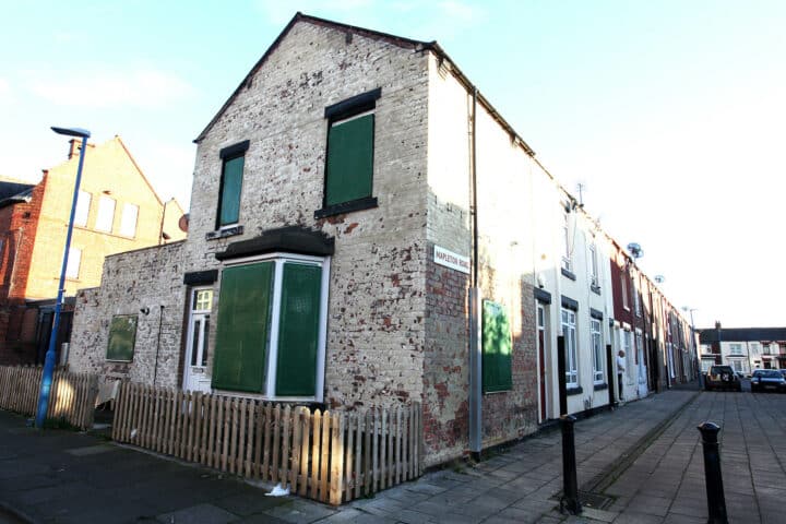 A painted house with boarded up windows at the end of a street.