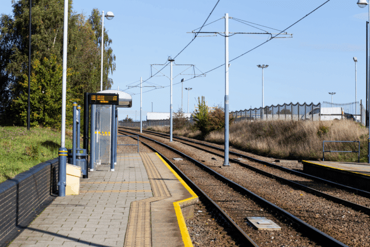 A tram station platform with a covered seating area. It is a bright, sunny day.